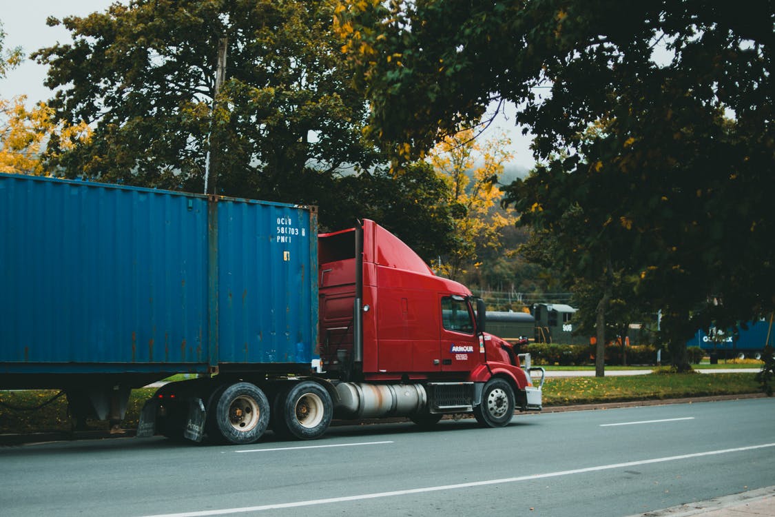 A red truck carrying a blue container makes its way down the road. 